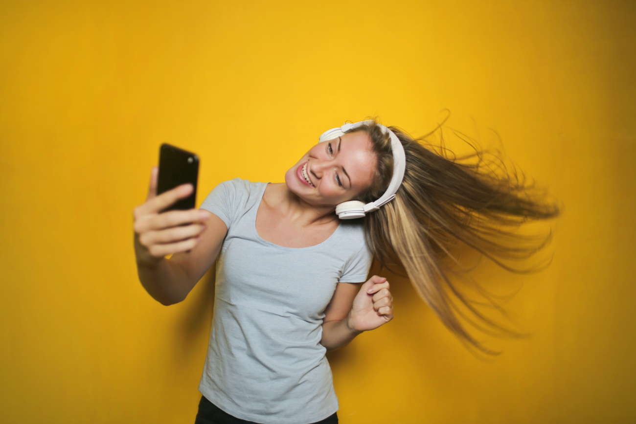 woman with headphone recording selfie video on yellow backdrop