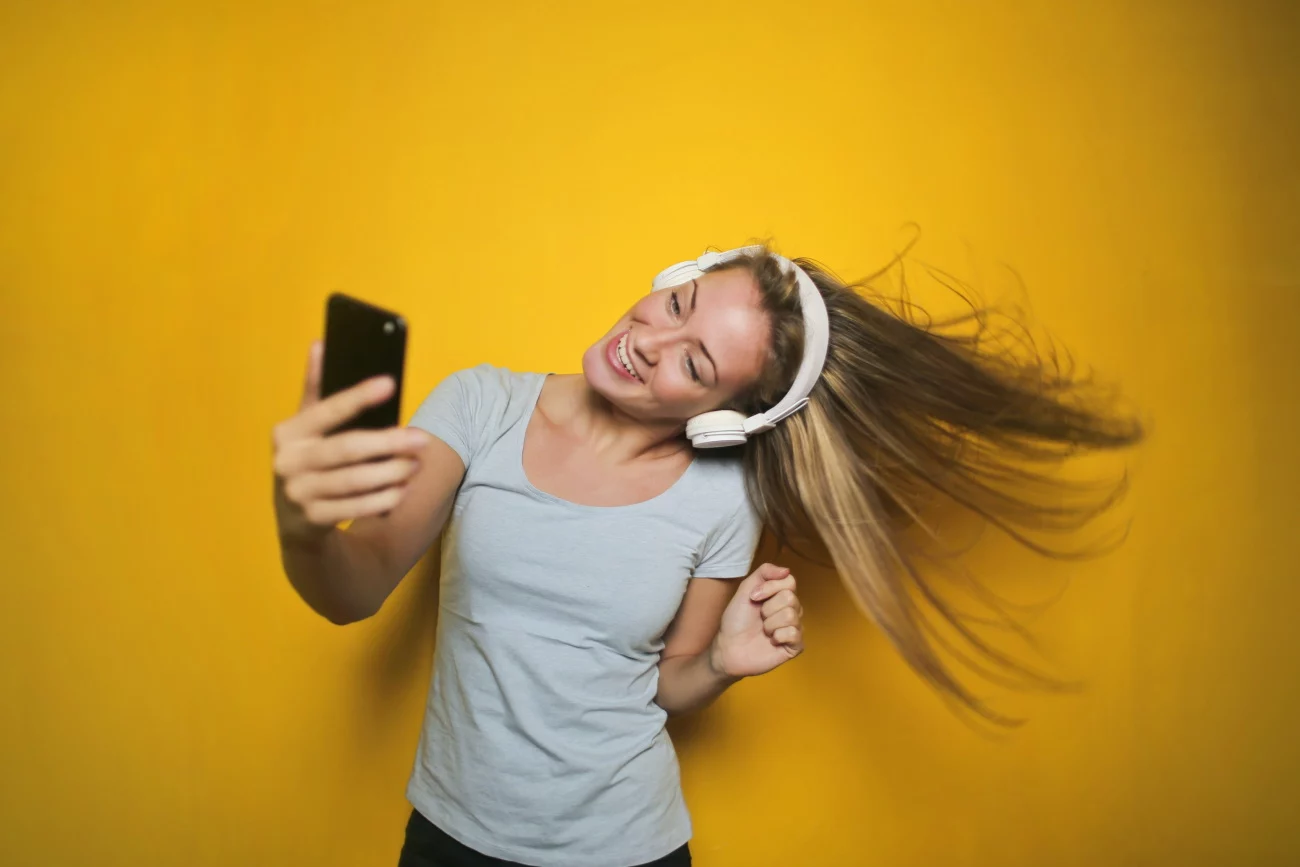 woman with headphone recording selfie video on yellow backdrop