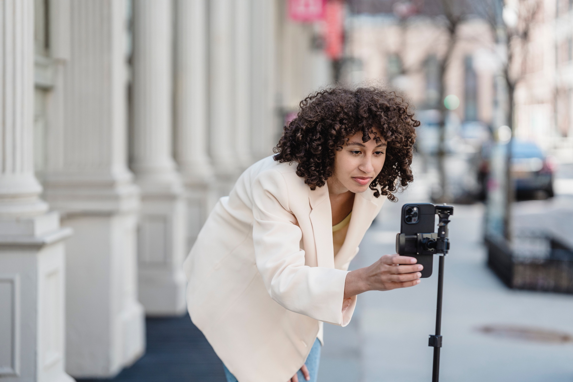 female wearing blazer setting up phone to film on phone stand outdoors